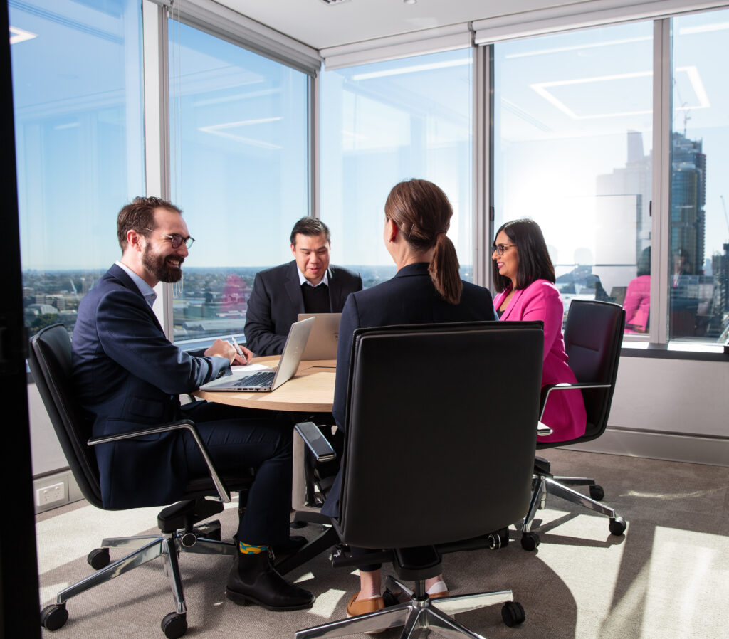 four people in meeting room at round table working and smiling