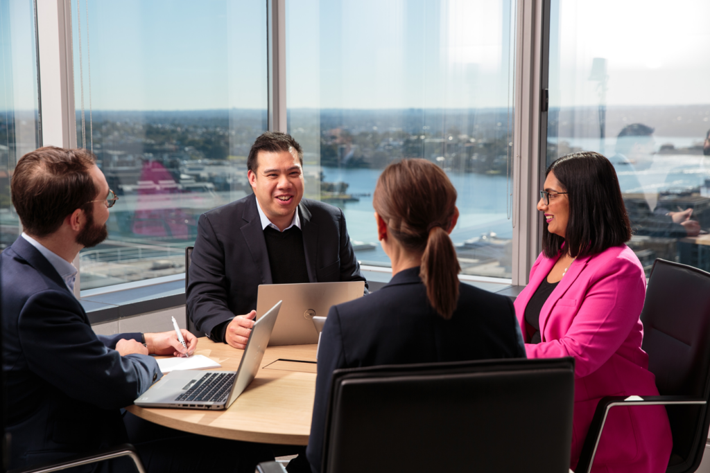 Group of professionals sat around a table having a meeting, with view of water and buildings in the background